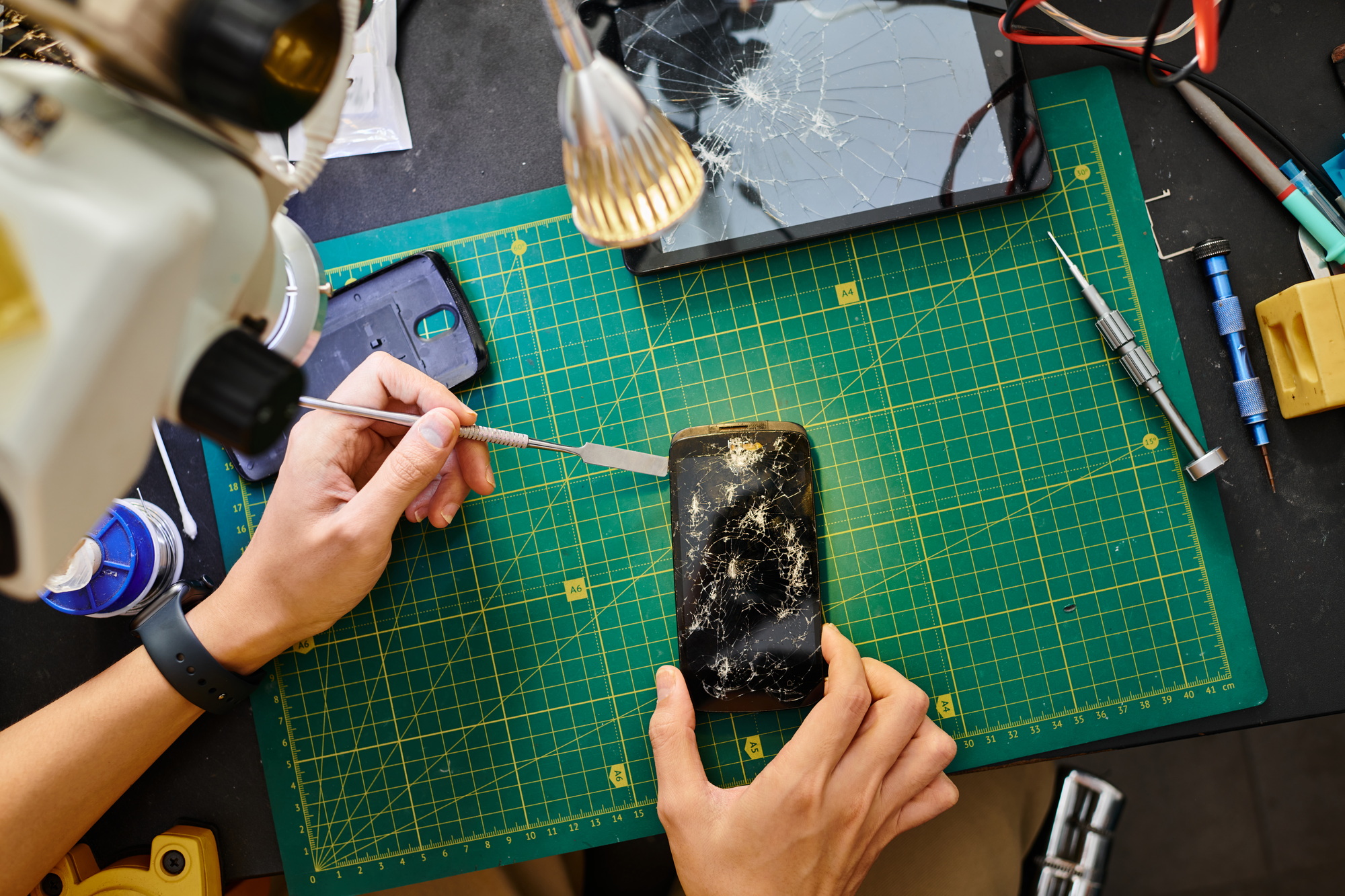 cropped view of repairman removing broken touchscreen of smartphone in maintenance workshop